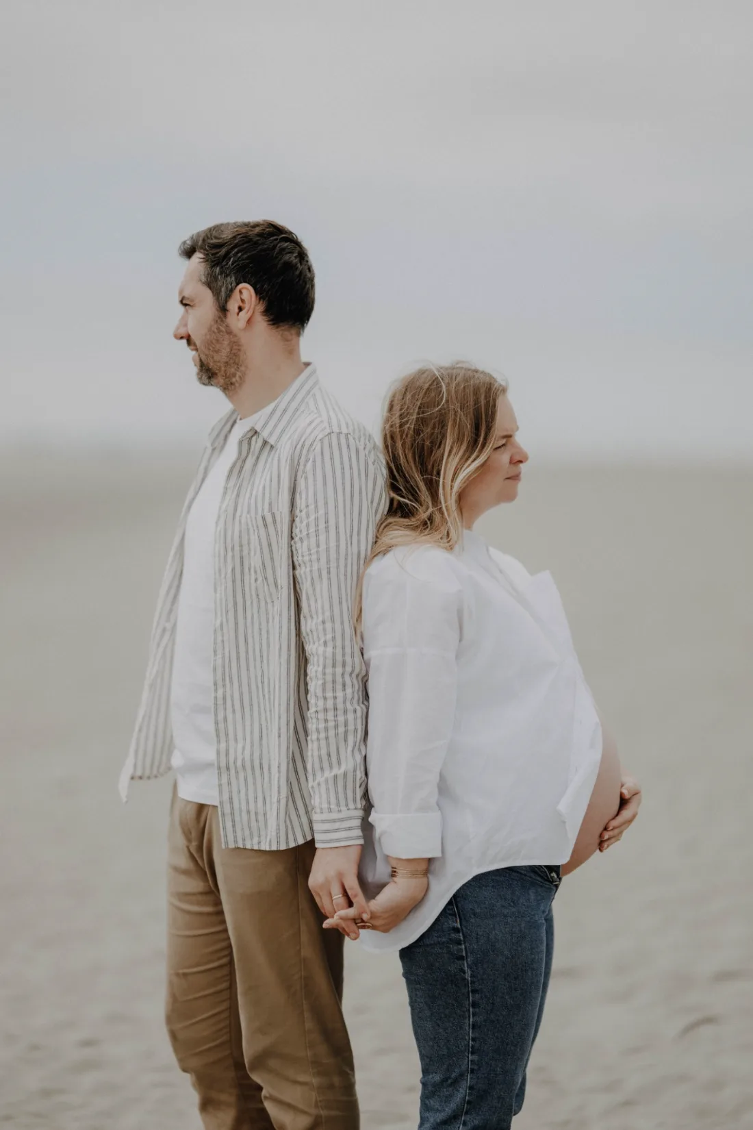 Future maman et son compagnon dos à dos, main dans la main, séance grossesse sur la plage de Merlimont