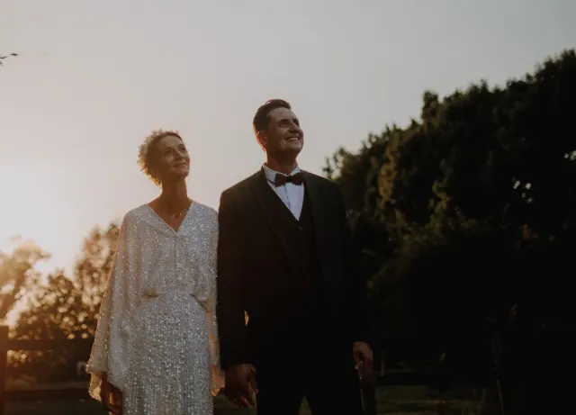 Mariés main dans la main au coucher du soleil, le regard levé vers le ciel, séance couple dans les Weppes