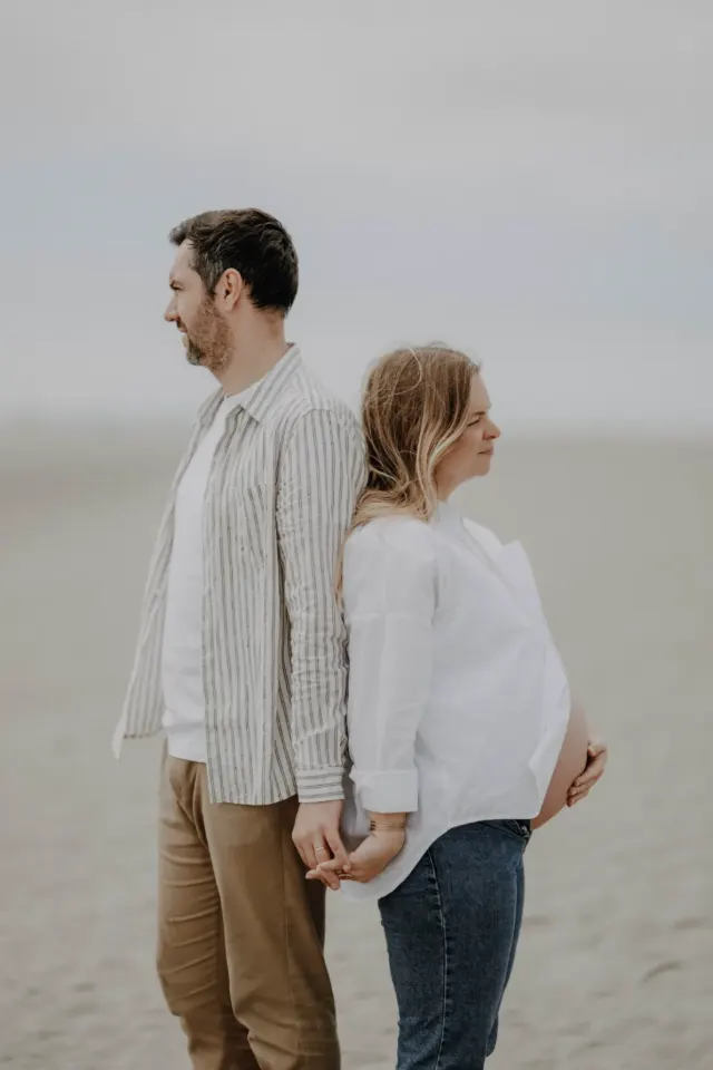 Future maman et son compagnon dos à dos, main dans la main, séance grossesse sur la plage de Merlimont