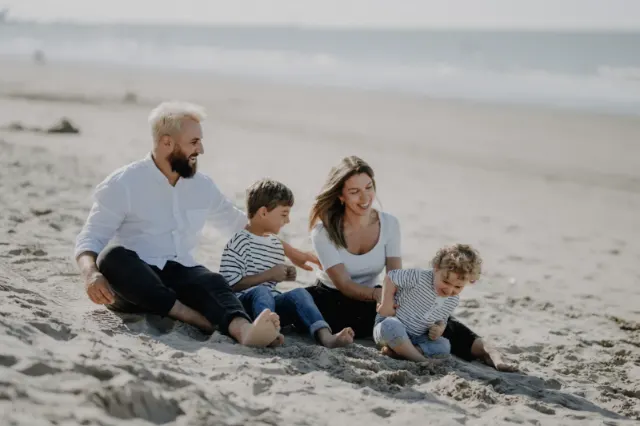 Parents et leurs deux garçons en marinière assis dans le sable, séance famille sur la plage de Leffrinckoucke