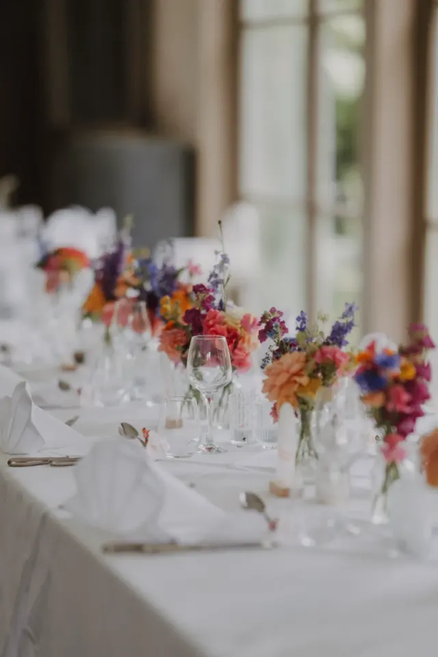 Table de réception dressée de petits bouquets de fleurs colorées, au Domaine des Bouleaux à Seneffe