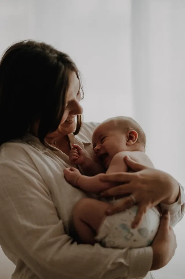 Maman tenant contre elle son bébé qui éclate de rire, séance naissance à domicile à Dunkerque