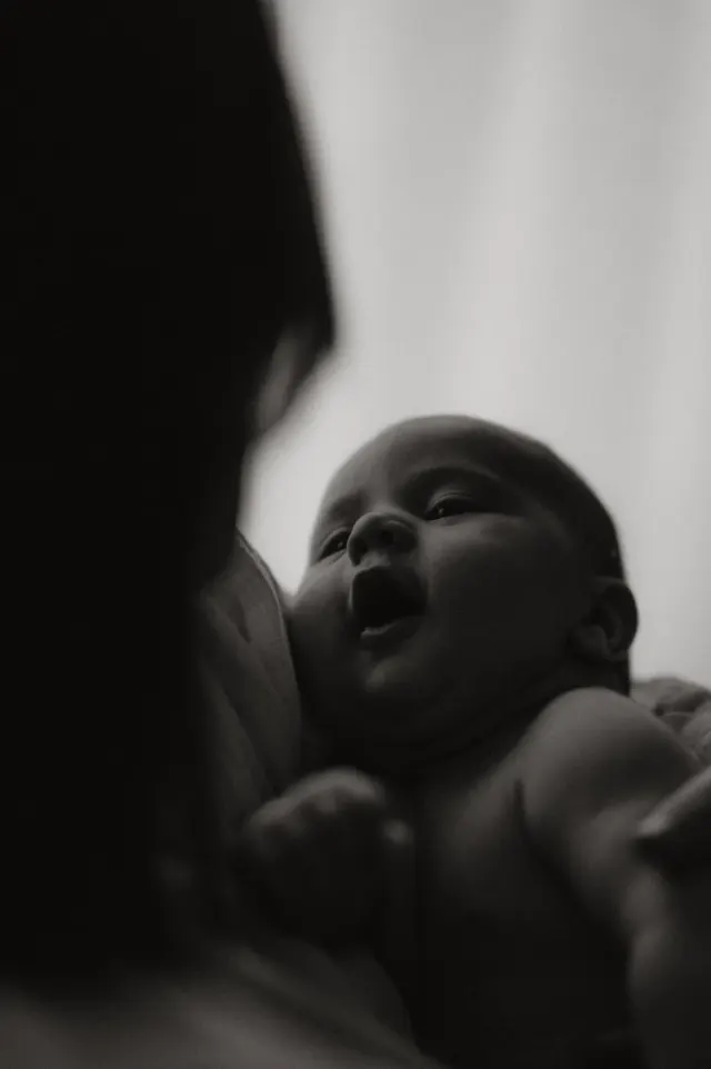Bébé blotti contre sa maman, le regard levé, en noir et blanc, séance naissance à domicile à Dunkerque
