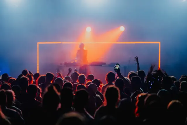 Public en contre-jour devant un DJ baigné de lumière orange et de fumée, En Nord Beat Festival à Bailleul