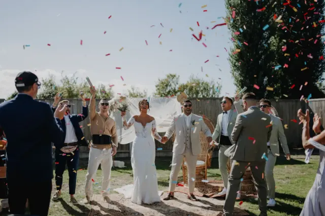 Mariés main dans la main sous une pluie de confettis, entourés de leurs amis aux lunettes de soleil qui explosent de joie, mariage au 't Groot Moerhof à La Panne