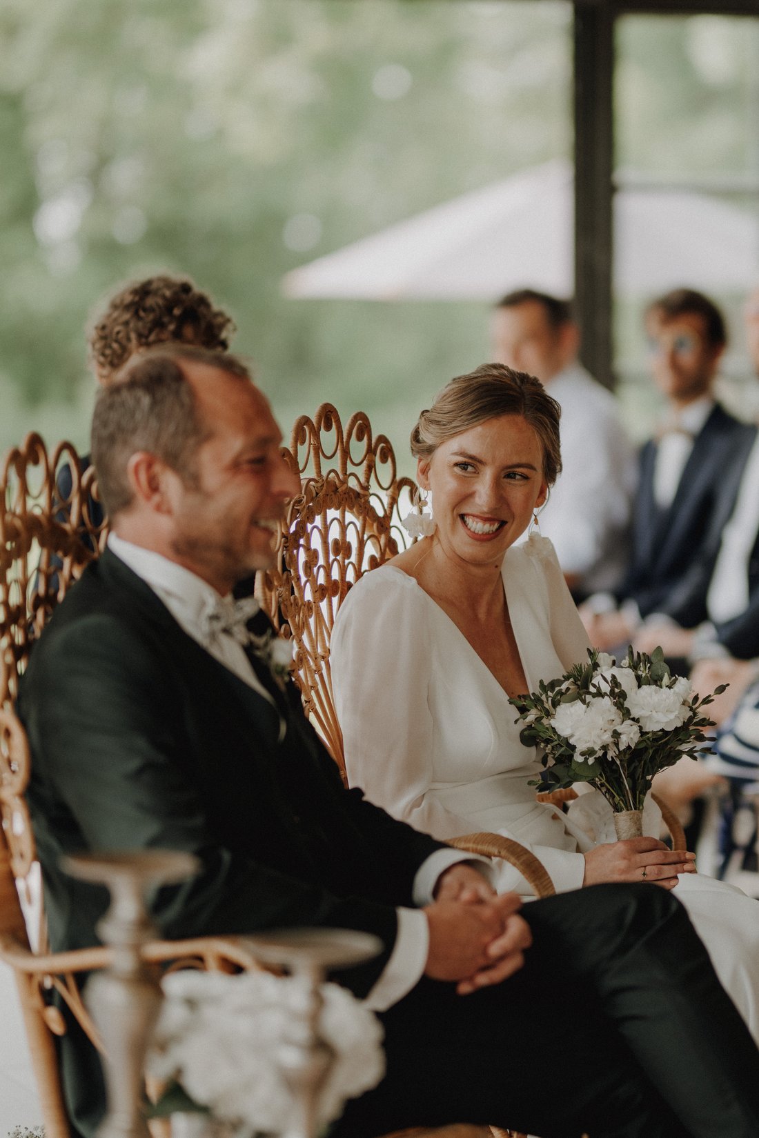 Mariée souriante assise sur un fauteuil en rotin pendant la cérémonie — mariage bohème Nord