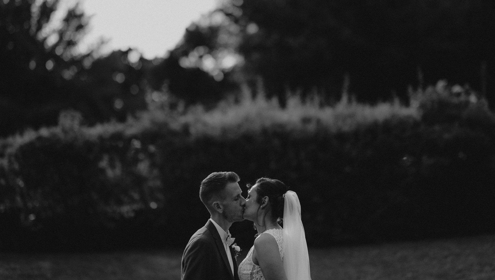 Baiser tendre des mariés en noir et blanc devant une haie en plein air — séance couple lifestyle, Hauts-de-France