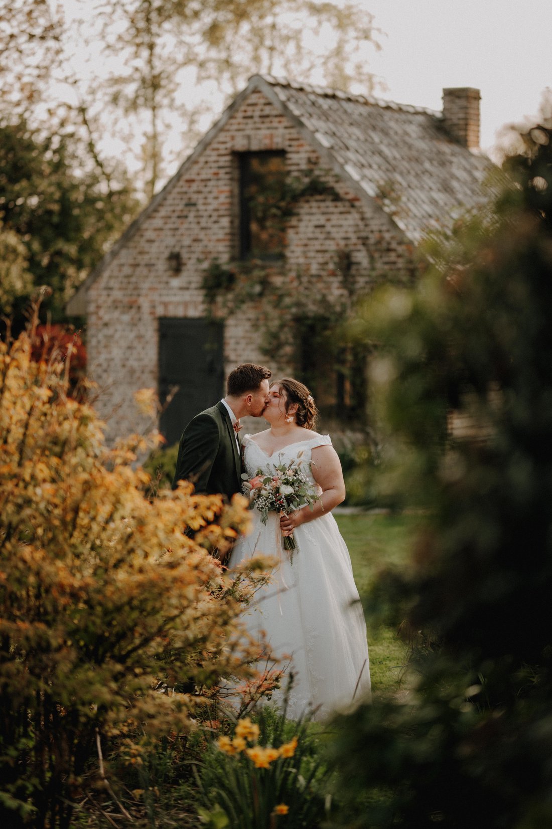 Baiser des mariés devant une longère en briques fleurie — mariage automnal Flandres